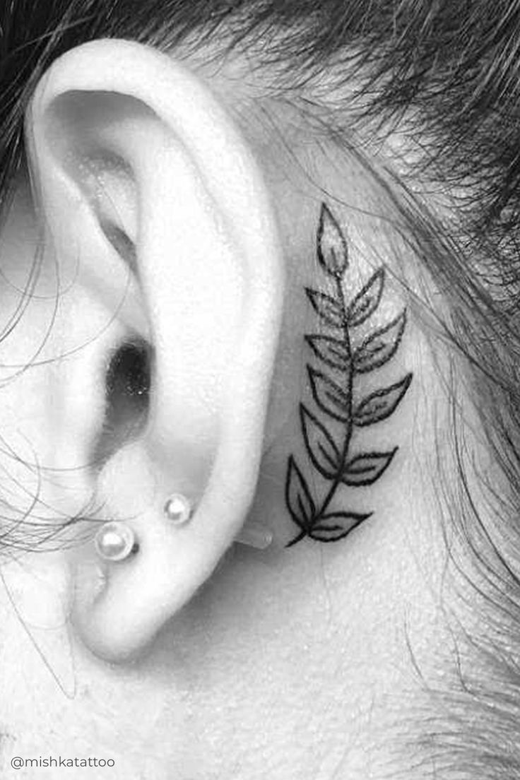 a woman's behind the ear with a small leaf tattoo on it