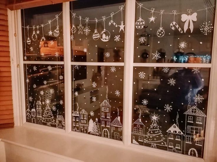 a window with christmas decorations drawn on the glass and snowflakes hanging from it