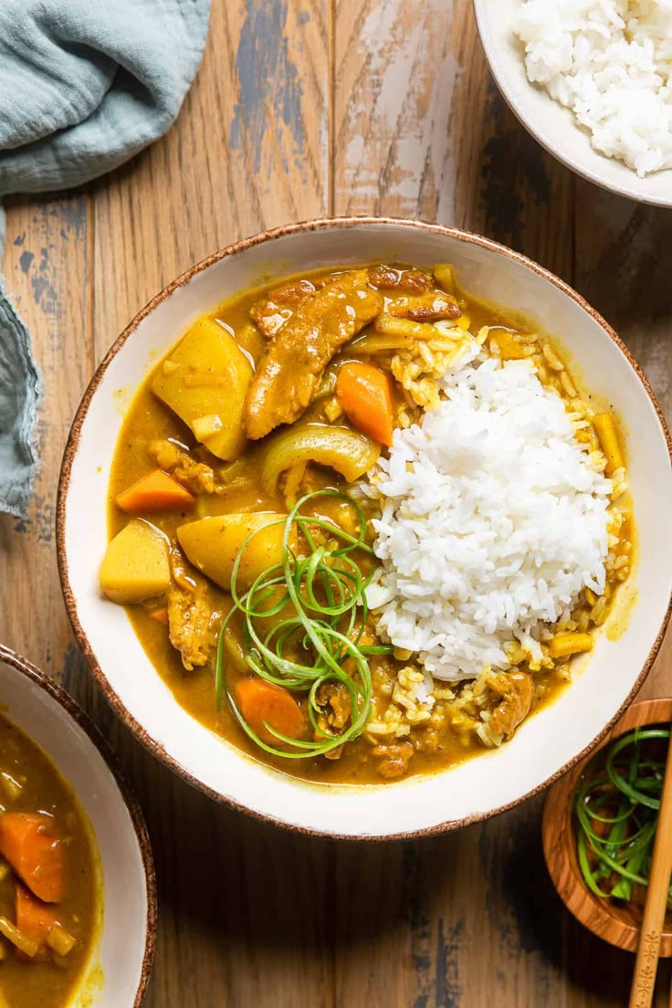 two bowls filled with curry, rice and carrots on top of a wooden table