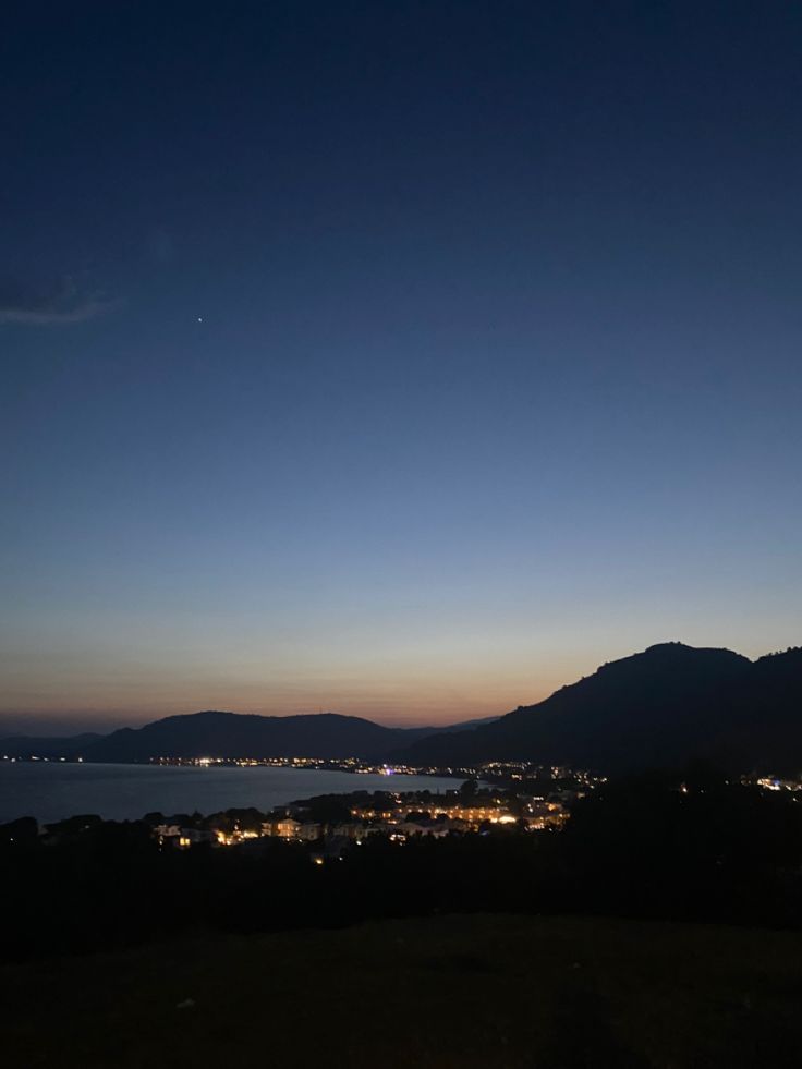 the night sky is lit up with bright lights and mountains in the distance are seen