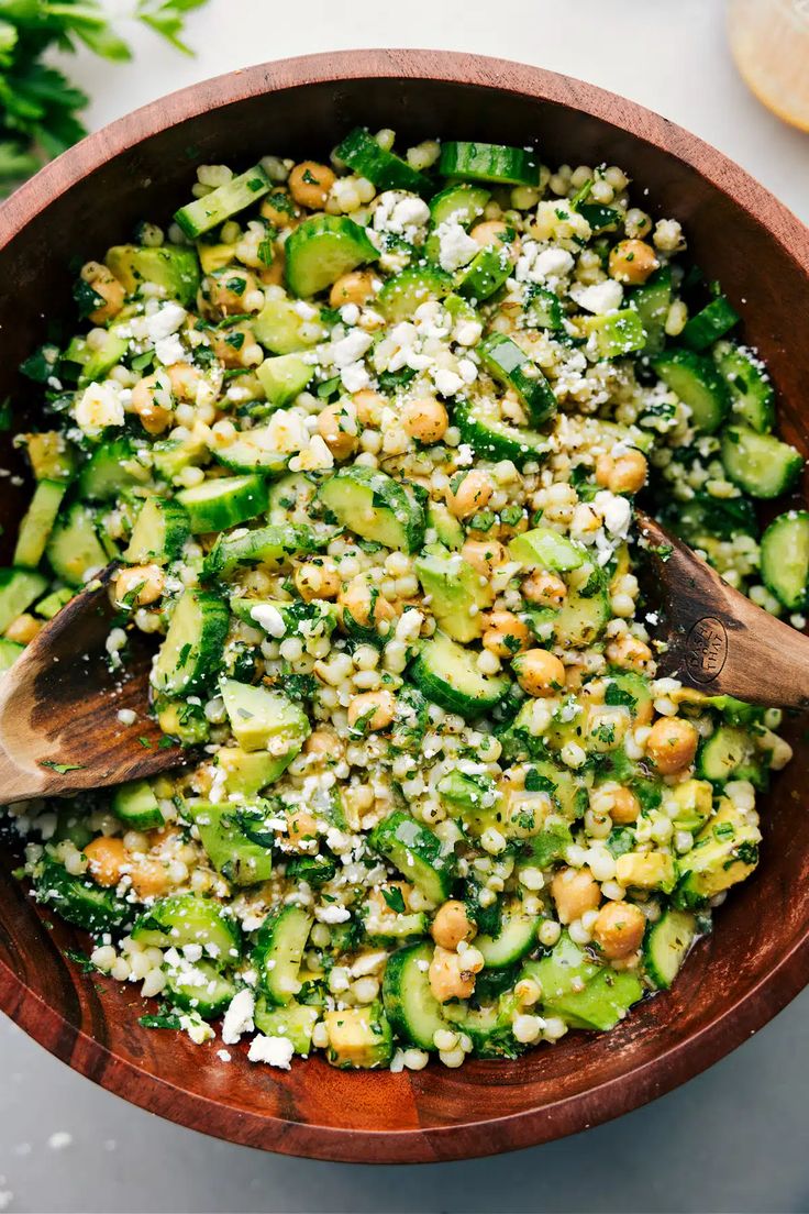 a wooden bowl filled with cucumber and chickpeas salad on top of a white table