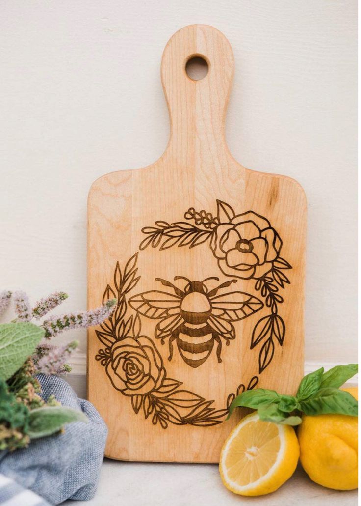 a cutting board with a bee on it next to some lemons and flowers,