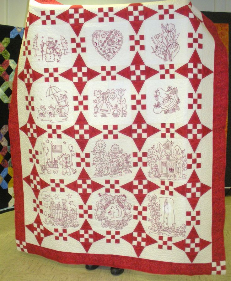 a large red and white quilt with many different designs on it, sitting on top of a table