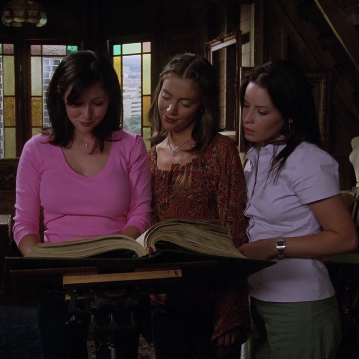 three women looking at an open book in a room with stained glass windows on the walls