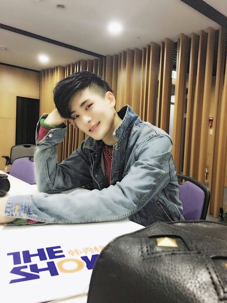 a young man sitting at a table with his hand on his head while looking off to the side