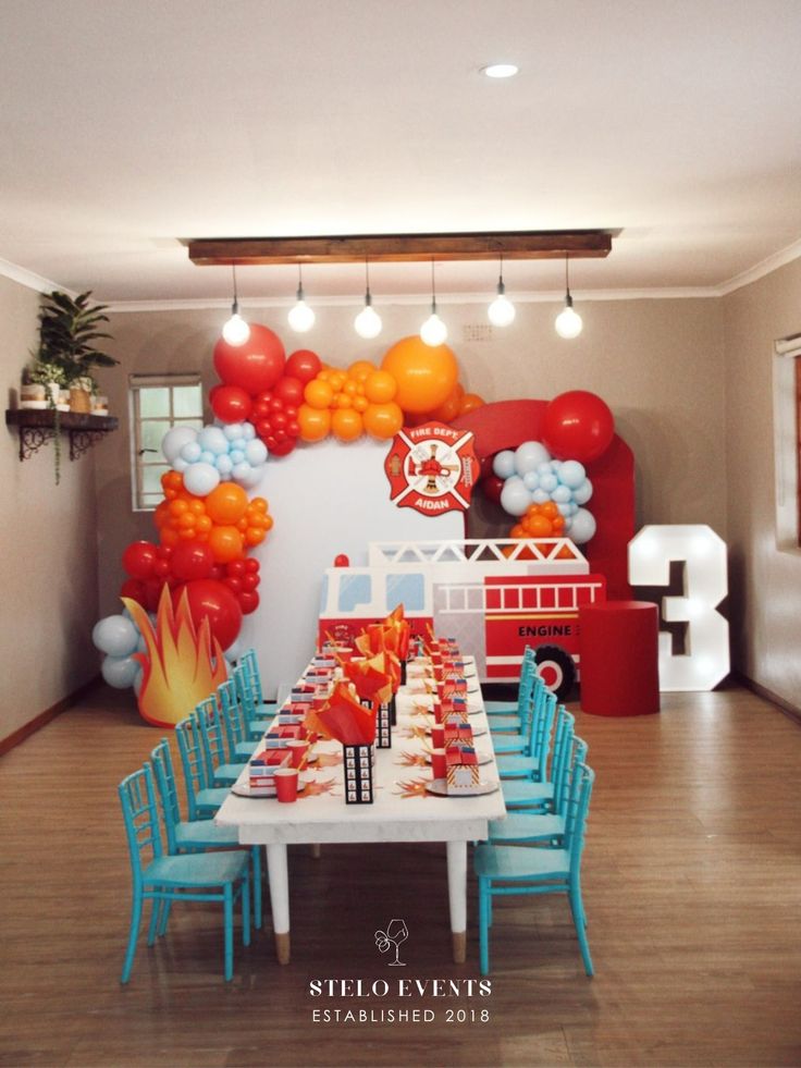 a table set up with balloons and firetrucks on the wall behind it