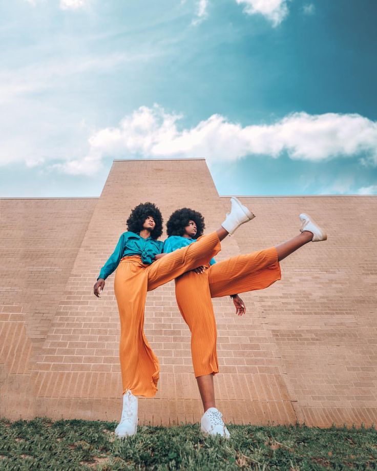 two women in orange pants and white shoes are standing on one leg with their arms around each other