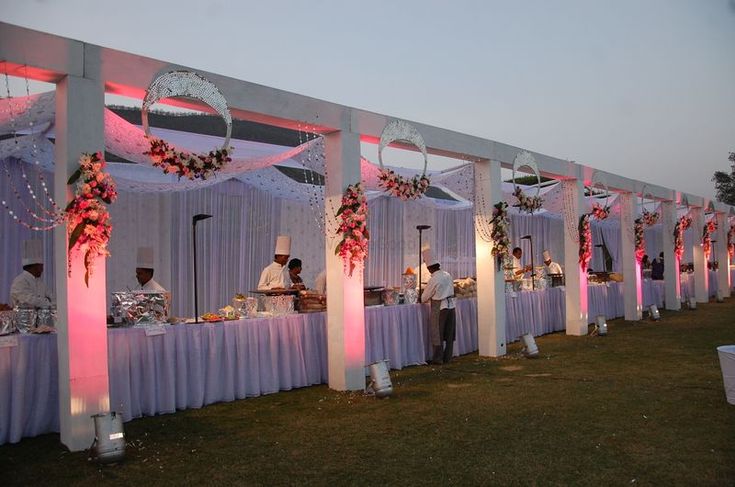 an outdoor banquet setup with white linens and pink flowers on the tables, along with other decorations