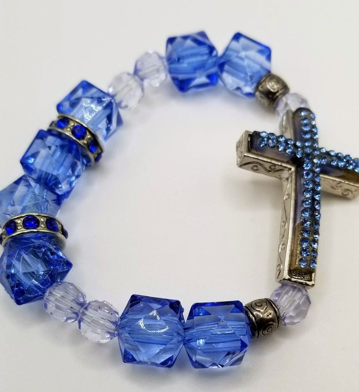 Upgrade your style with the elegant and beautiful Handcrafted Jewelry By Teri C Blue Cross Bracelet. This stunning bracelet features a light blue rhinestone cross. Wear it alone or layer it with other pieces for a unique look. This unique bracelet is perfect for any occasion and is sure to be an eye-catching addition to your jewelry collection. Blue Cross Spiritual Jewelry, Blue Spiritual Cross Jewelry, Blue Cross Bracelets As Gift, Blue Cross Bracelets For Gifts, Adjustable Blue Rosary Bracelet With Cross, Adjustable Blue Cross-shaped Jewelry, Trendy Jewelry Ideas, Rhinestone Cross, Blue Cross