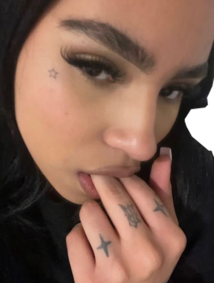 a close up of a person with tattoos on her face and hand near her mouth