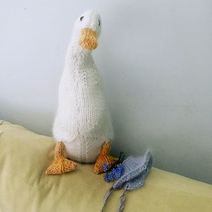 a knitted duck sitting on top of a bed next to two crocheted birds