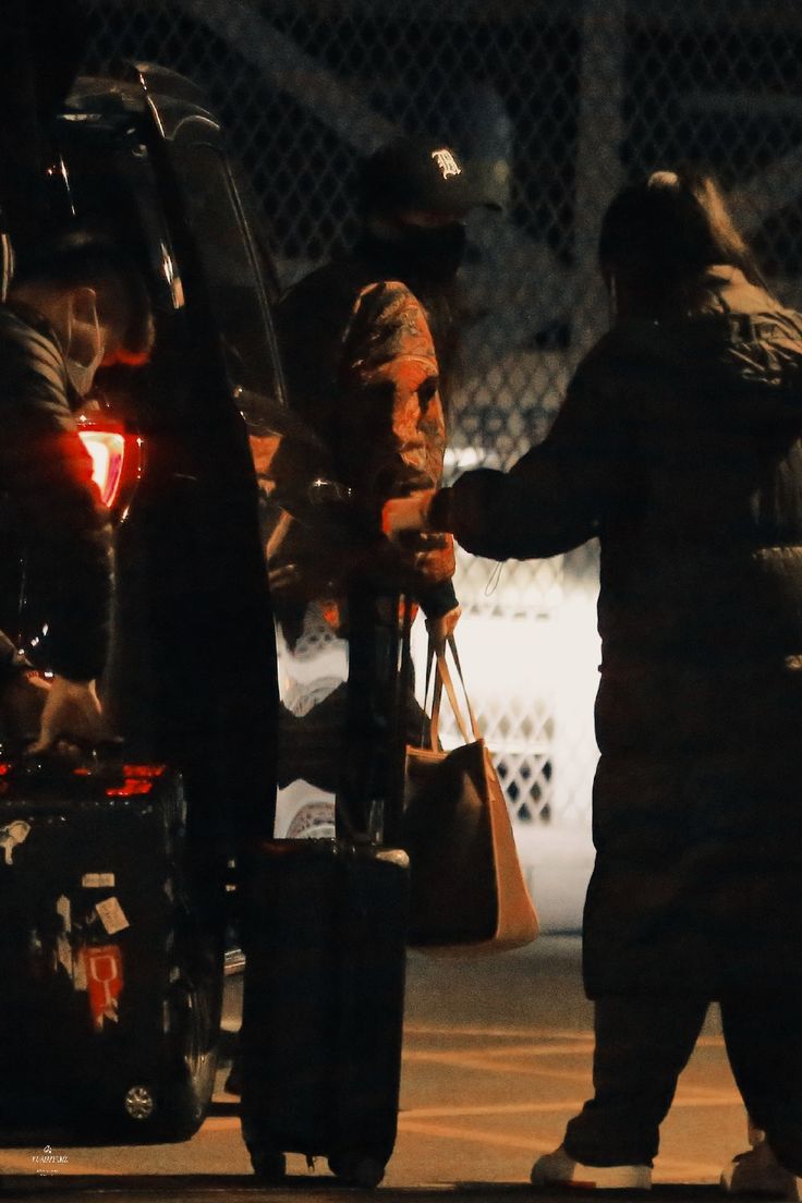 two people standing next to each other with luggage in their hands and one person holding the door open