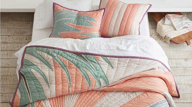 a bed with an orange and green comforter on top of it next to pillows