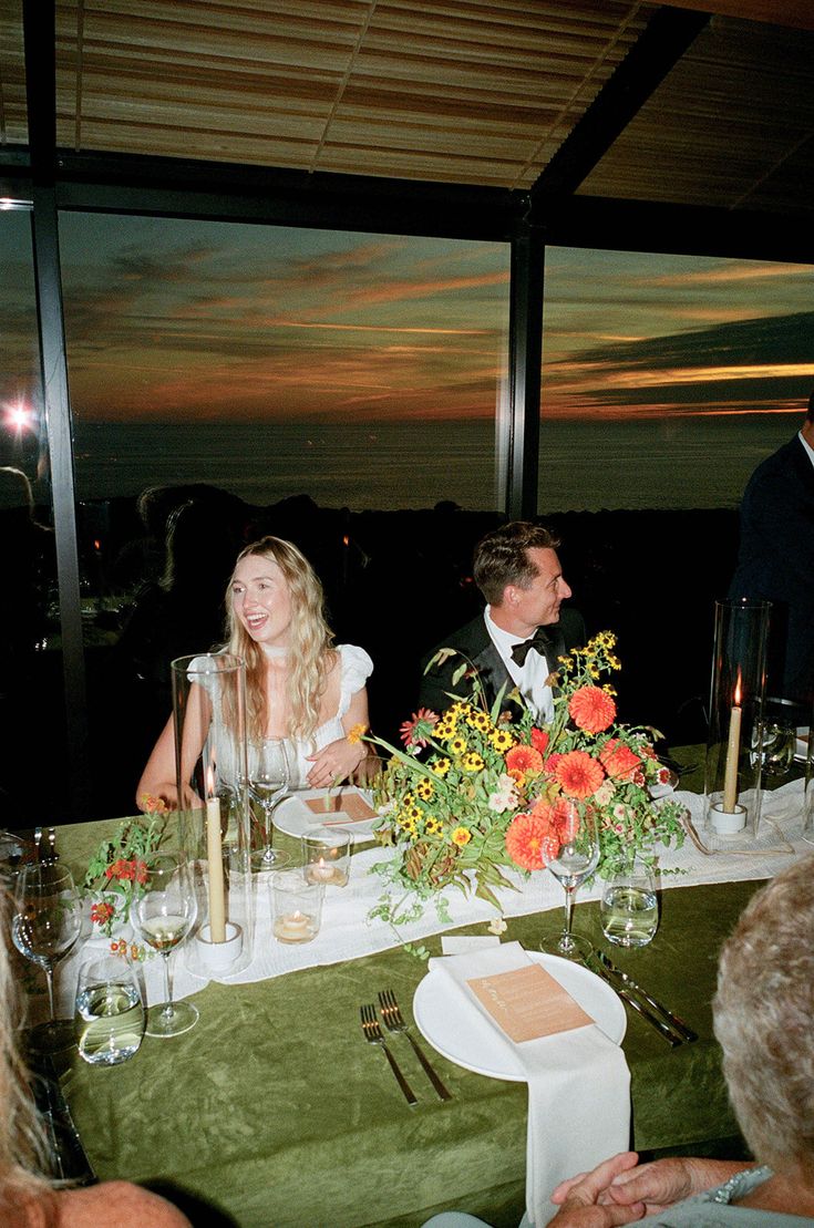 two people sitting at a table with flowers in vases and candles on the table