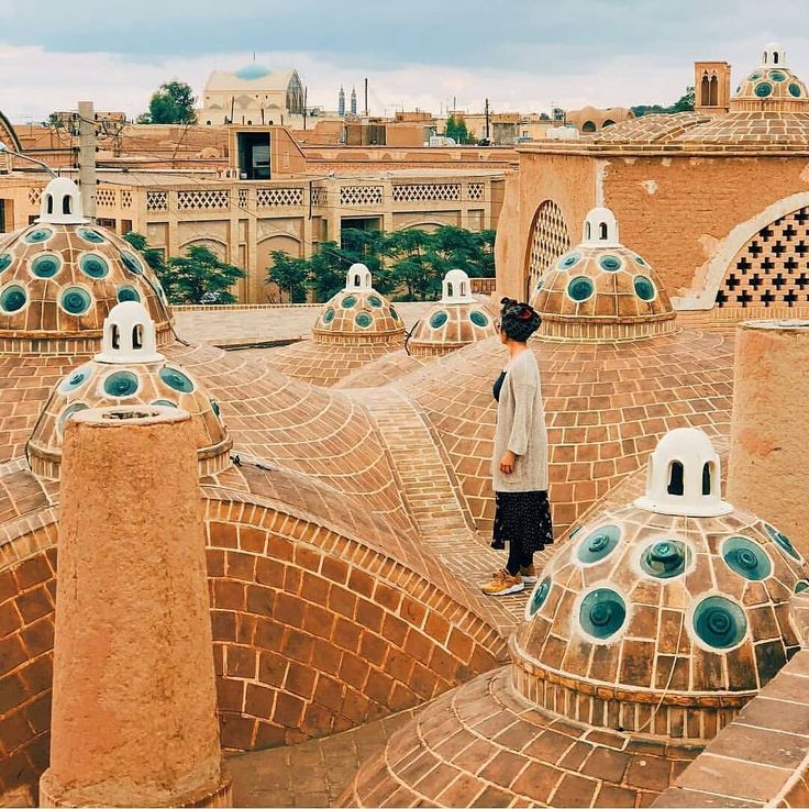 a man standing on top of a roof in the middle of an old city with blue and white domes