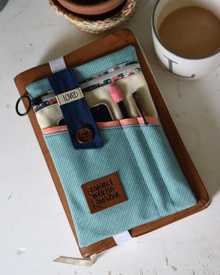 a cup of coffee sitting next to a blue case with makeup brushes in it on top of a table