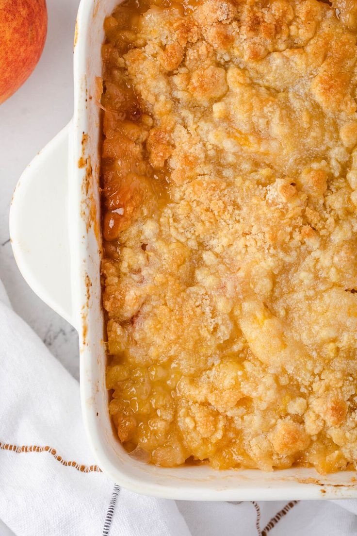 a casserole dish filled with peach cobbler next to an orange