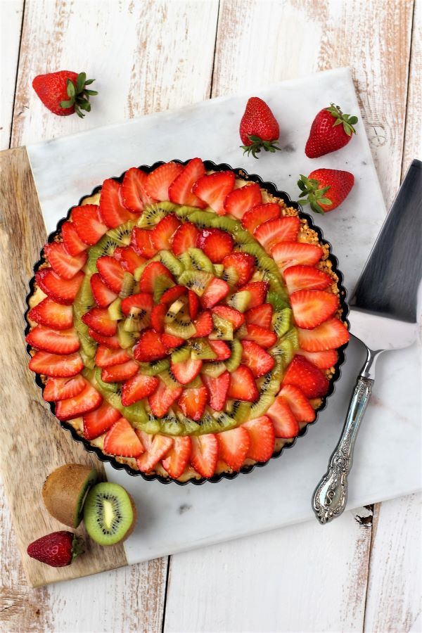 a pie with sliced strawberries and kiwis in it on a cutting board