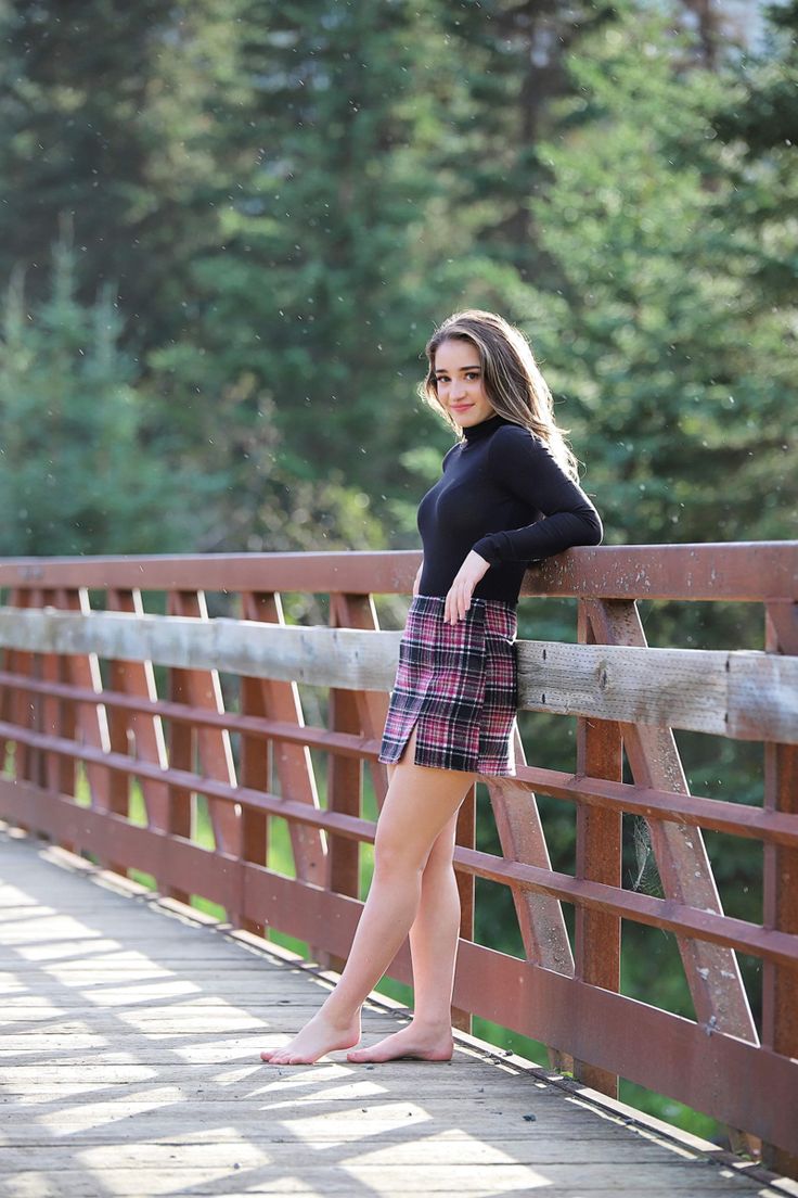 a beautiful young woman standing on a bridge posing for the camera with trees in the background