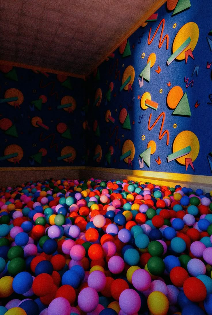 an indoor play area with lots of balls and colorful wallpaper on the walls behind it