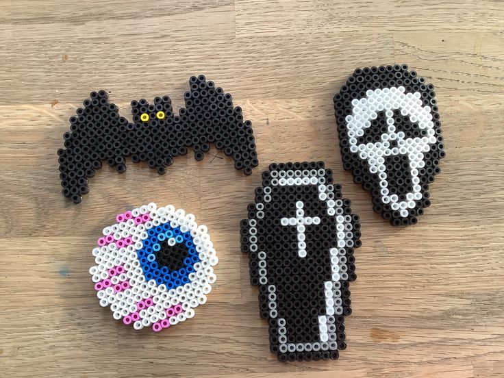 three pieces of bead art on a wooden surface, one with a skull and the other with a cross