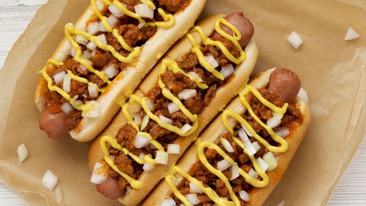 two chili dogs with mustard and onions on them