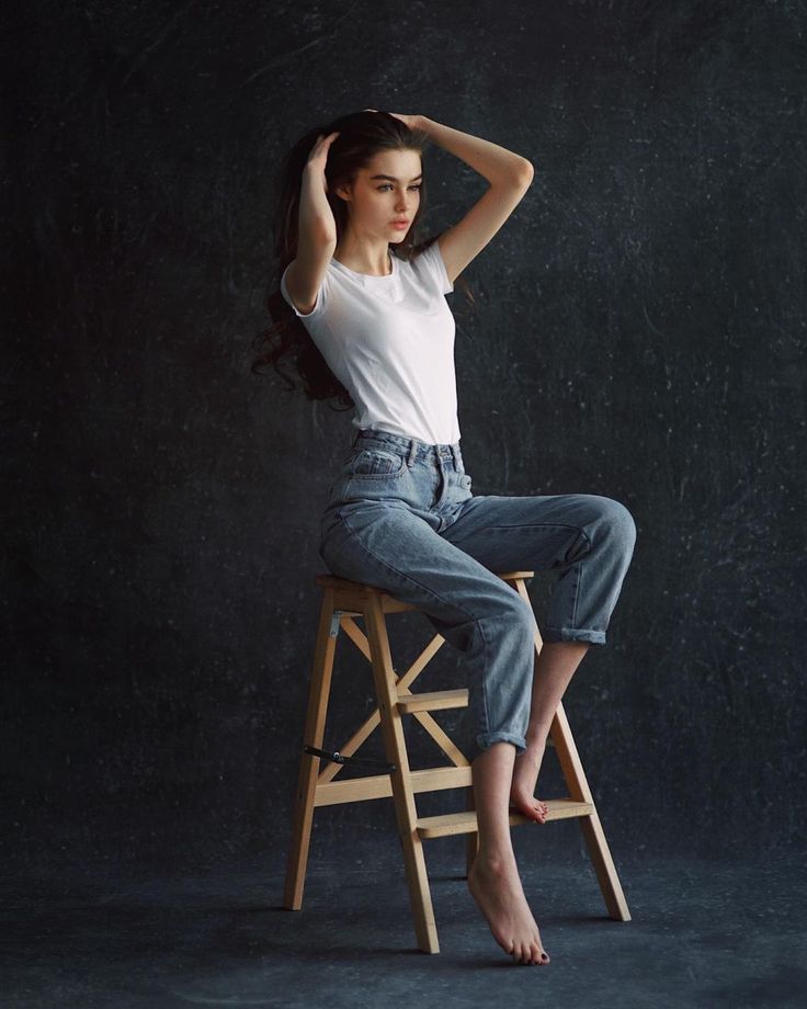 a young woman sitting on top of a wooden stool wearing jeans and white t - shirt