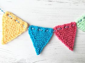 crocheted triangle bunting on a white wooden background with blue and yellow yarn