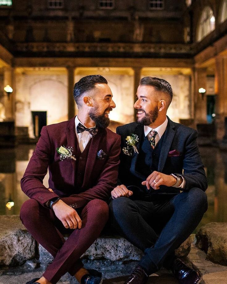 two men in suits sitting next to each other and smiling at each other's eyes