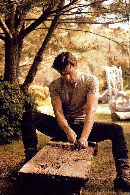 a man is sitting on a bench in the grass and tying his shoelaces