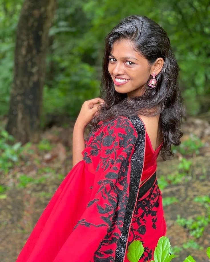 a woman wearing a red and black dress in the woods posing for a photo with her hand on her shoulder