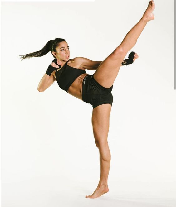 a woman in black shirt and shorts doing a kickbox pose with one leg up