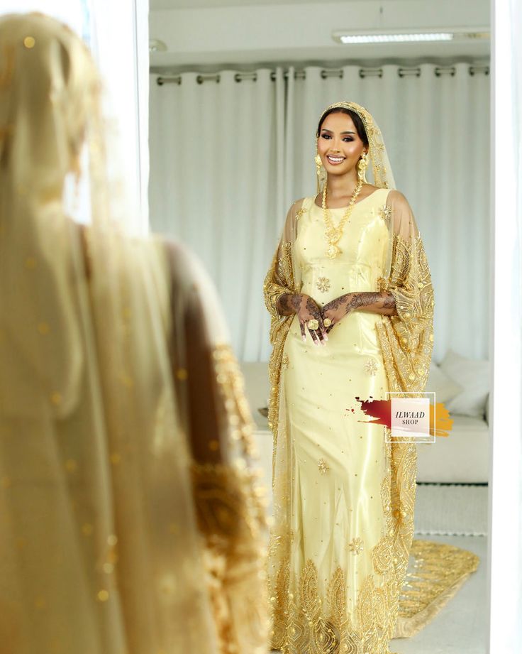 a woman standing in front of a mirror wearing a yellow dress and veil with gold sequins on it