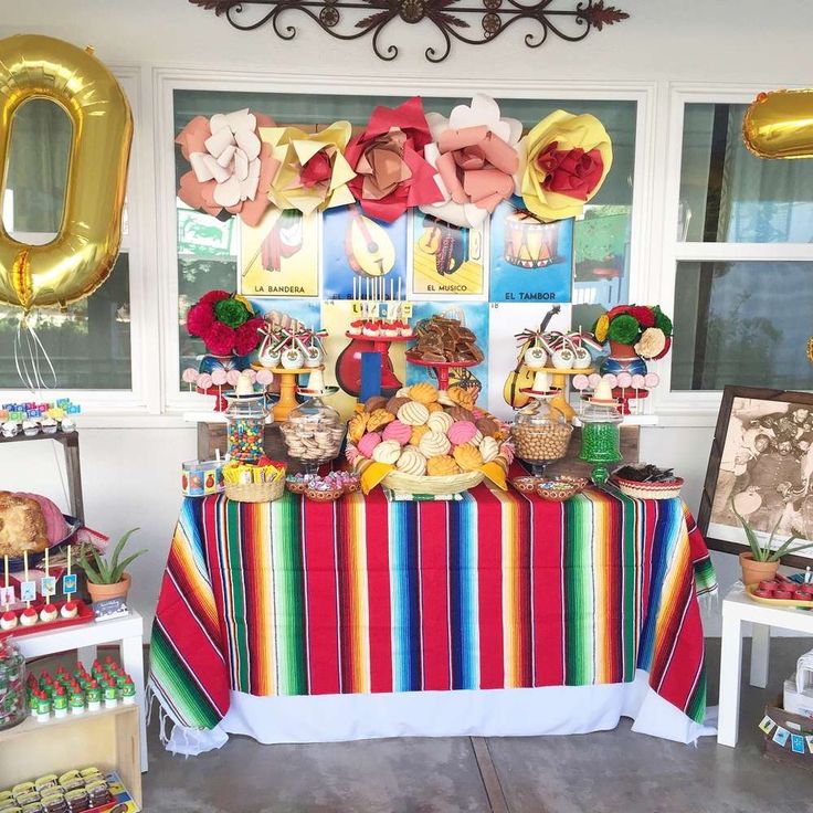 a colorful table topped with lots of desserts and balloons in front of a window