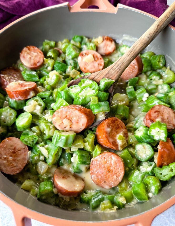 a skillet filled with sausage and green peppers on top of a table next to a purple towel