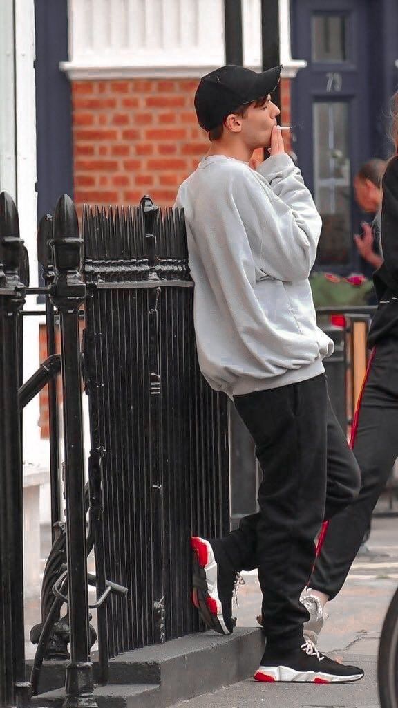 a young man leaning against a fence talking on his cell phone while walking down the street