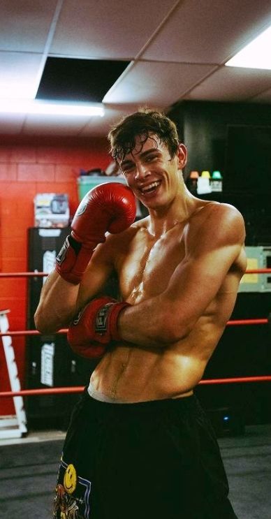 a shirtless man standing in a boxing ring with his hands on his hips and wearing red boxing gloves