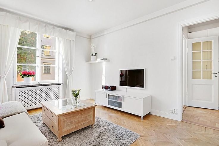 a living room with white walls and wood floors is pictured in this image, there is a television on the coffee table