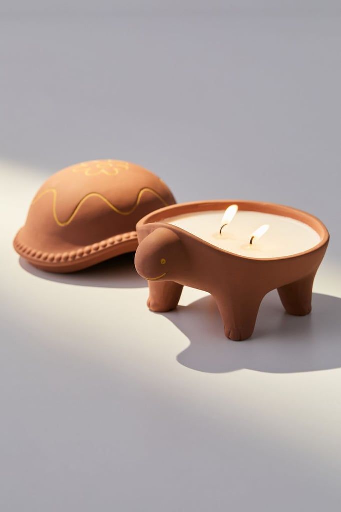 an elephant shaped candle holder next to a brown hat on a white surface with light coming from behind it