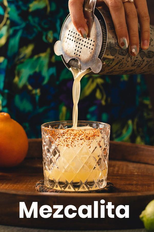 a person pouring something into a glass on top of a wooden table with oranges in the background