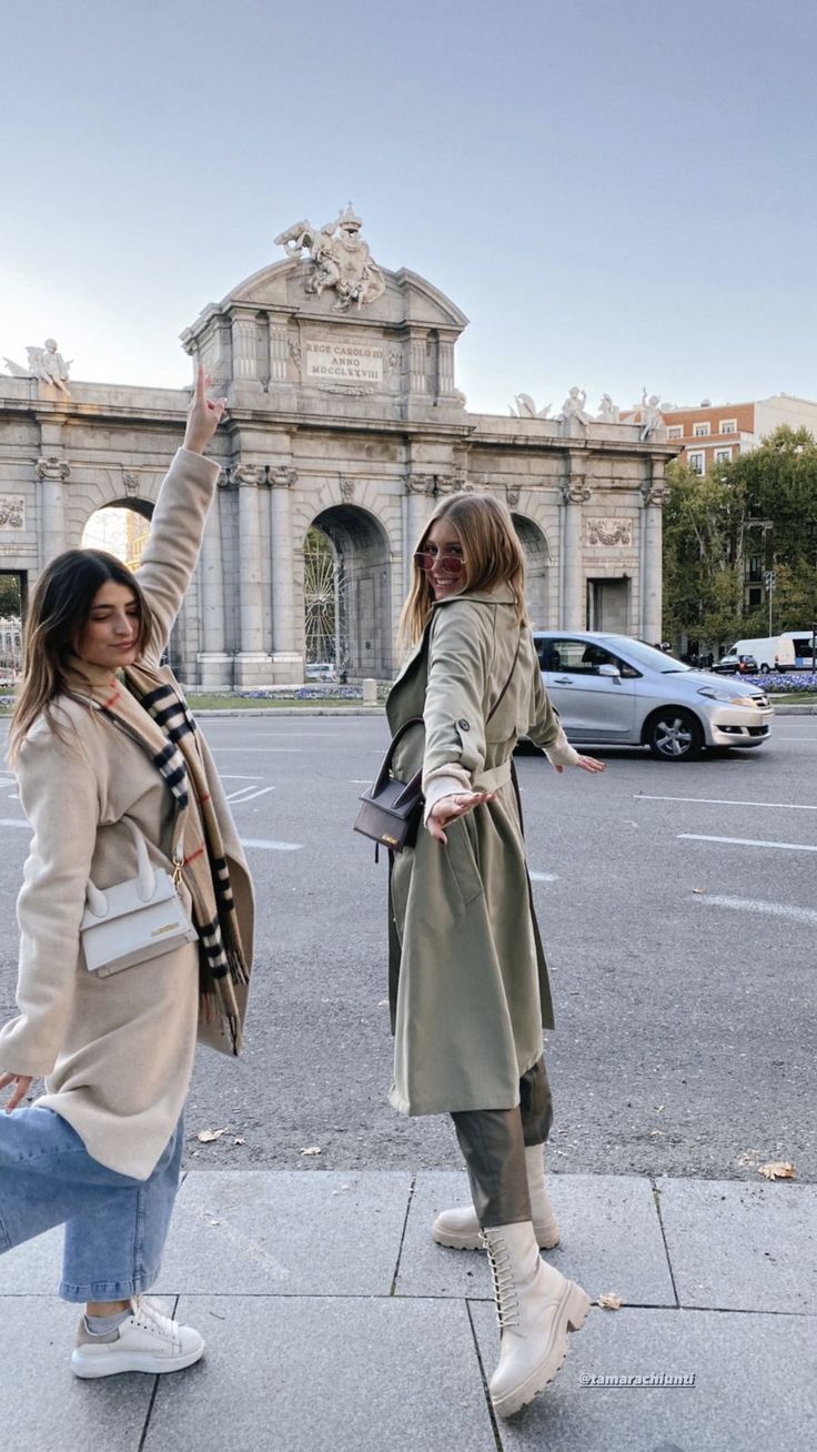 two women are standing on the sidewalk waving