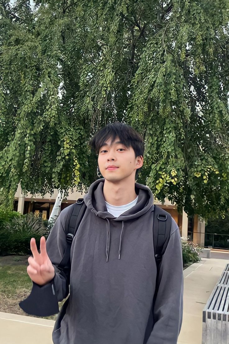 a young man standing in front of a tree giving the peace sign with his hand