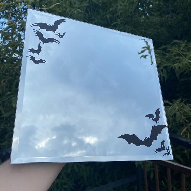 a hand holding up a mirror with bats on it and the sky in the background