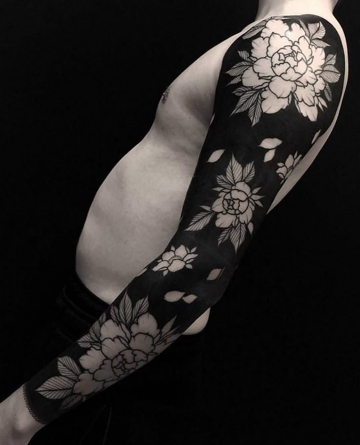 a man's arm covered in black and white tattoos with flowers on the sleeve