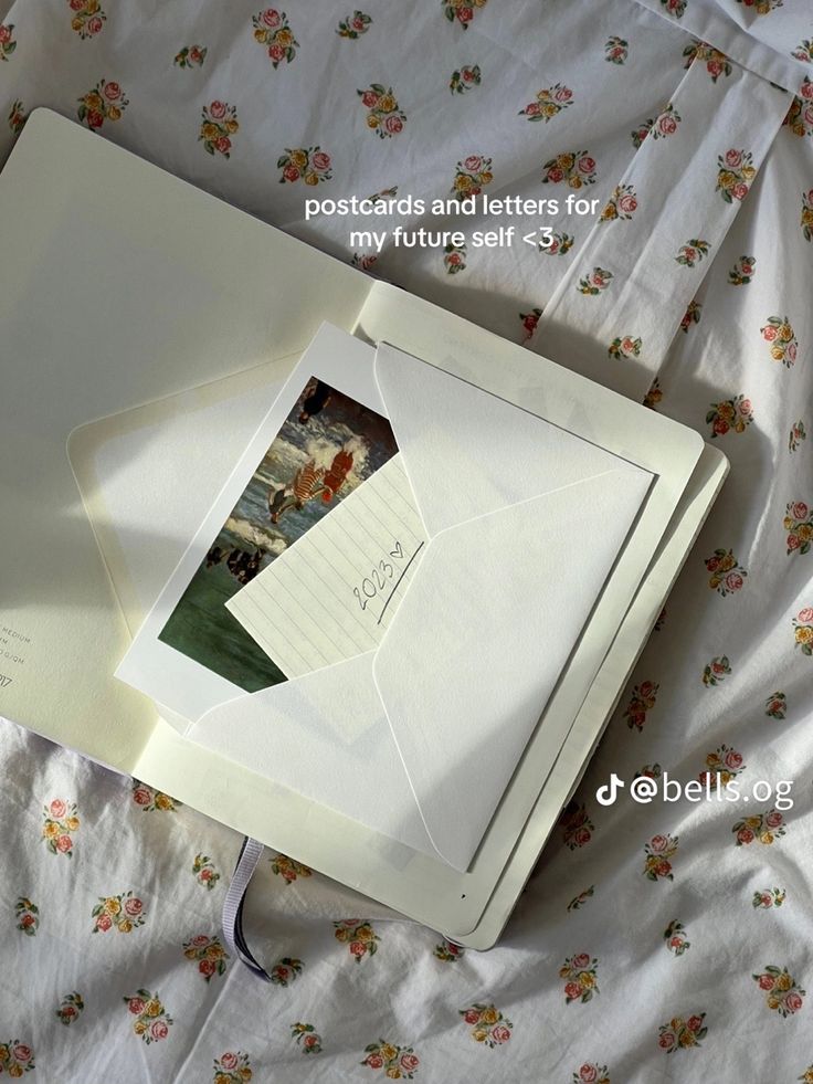 an open photo album on top of a bed with floral sheets and white envelopes