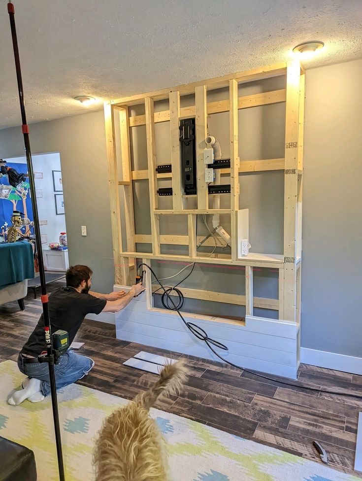 a man is working on an entertainment center in the living room, while his dog watches