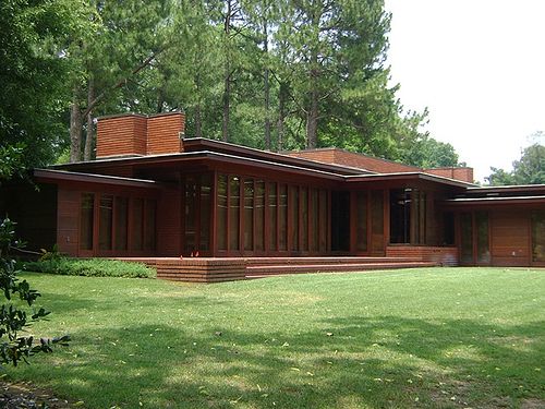 a large house sitting in the middle of a lush green field next to a forest