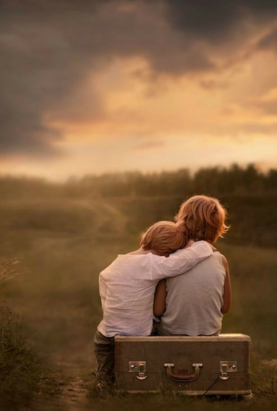 two people sitting on top of a piece of luggage in front of a cloudy sky