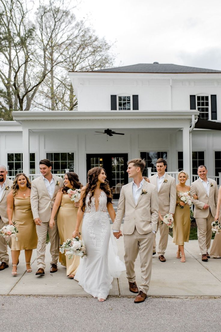 a bride and groom walking with their bridal party in front of a white house