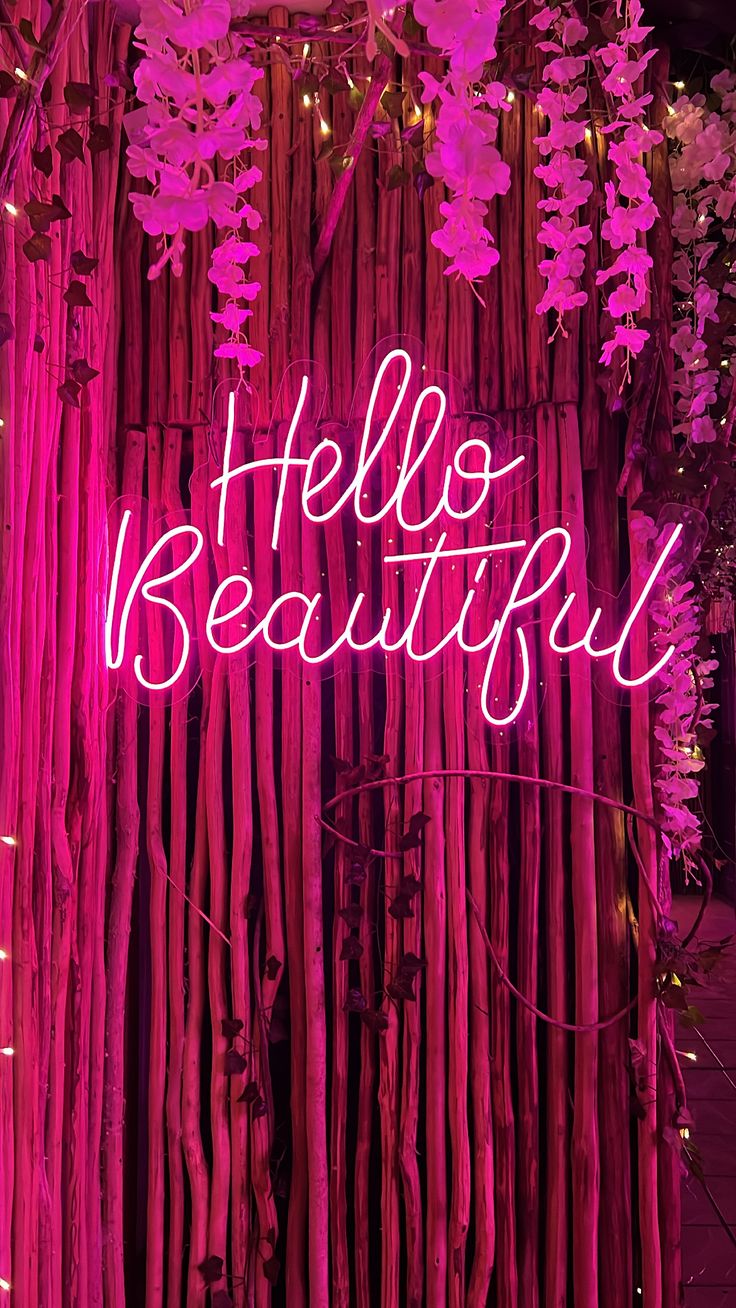 a pink neon sign that says hello beautiful in front of some bamboo stalks and flowers